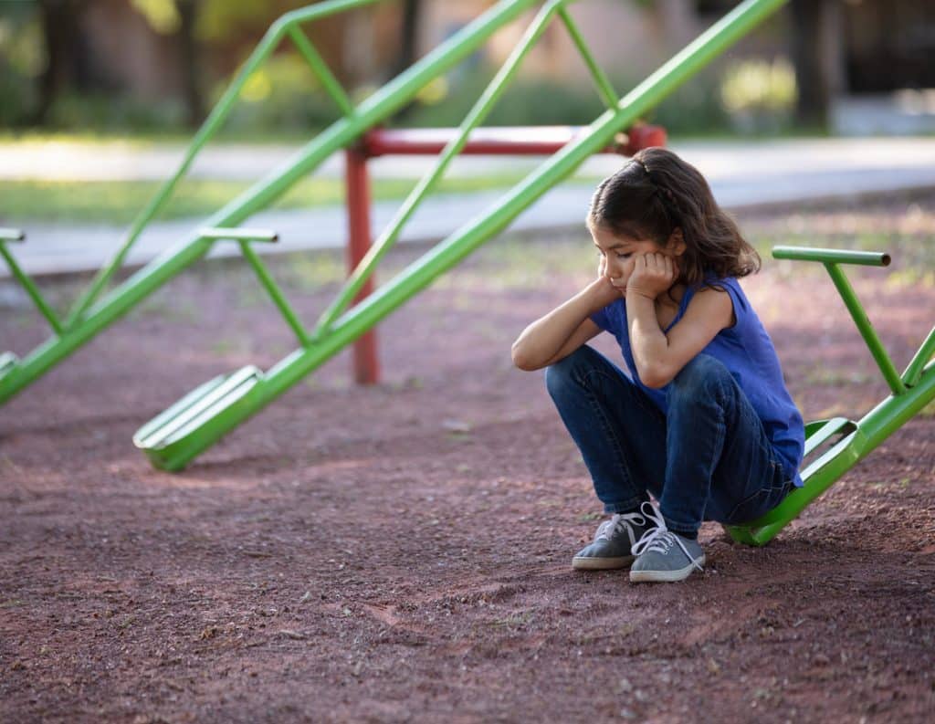 Girl with no one to play with on the teeter totter A sad little girl with incontinence sitting alone on a teeter tooter with her hands on her face.