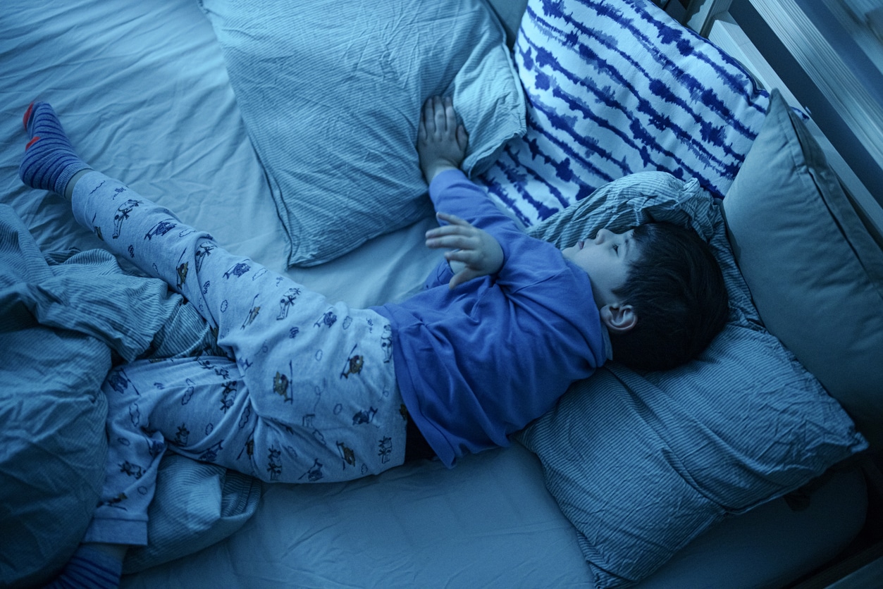 Little boy wriggle in his sleep and kicks off his blanket.